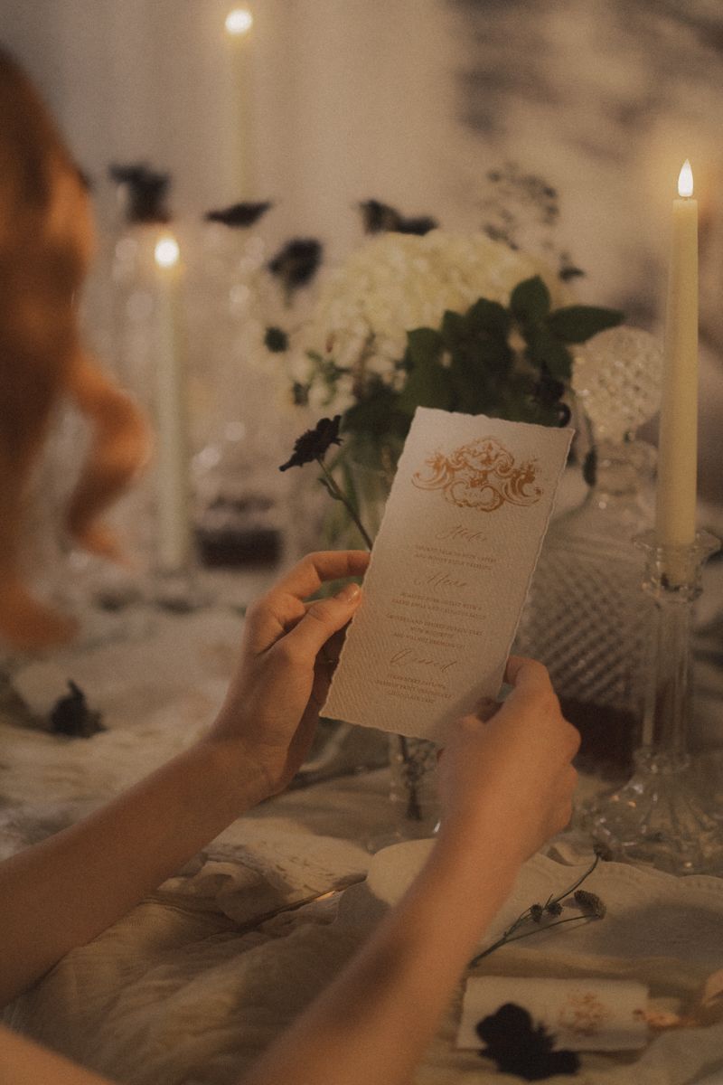 Hands holding an elegant wedding menu card at a candlelit reception table with romantic decor.