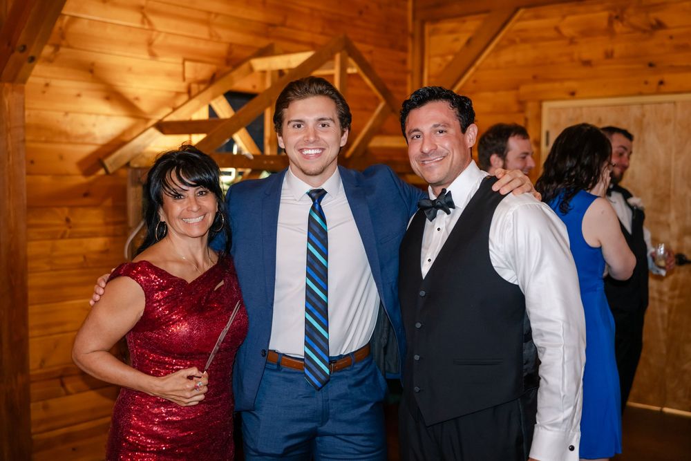 Three smiling guests pose together at a wedding reception in a rustic wood-paneled venue.