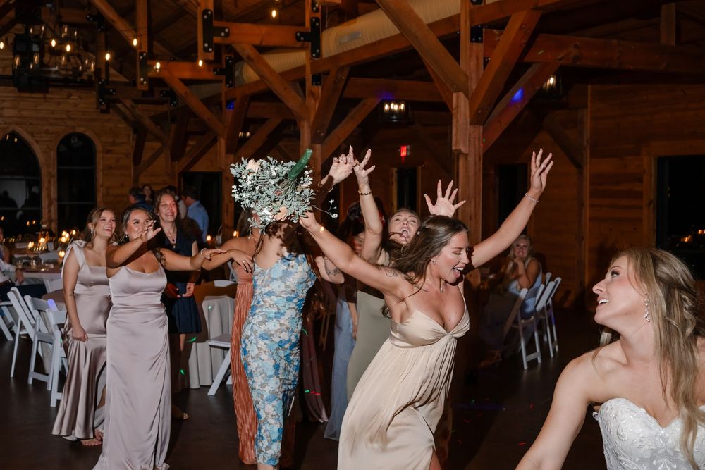 Wedding guests dancing joyfully at a rustic barn reception, with bridesmaids in gray gowns celebrating on the dance floor.