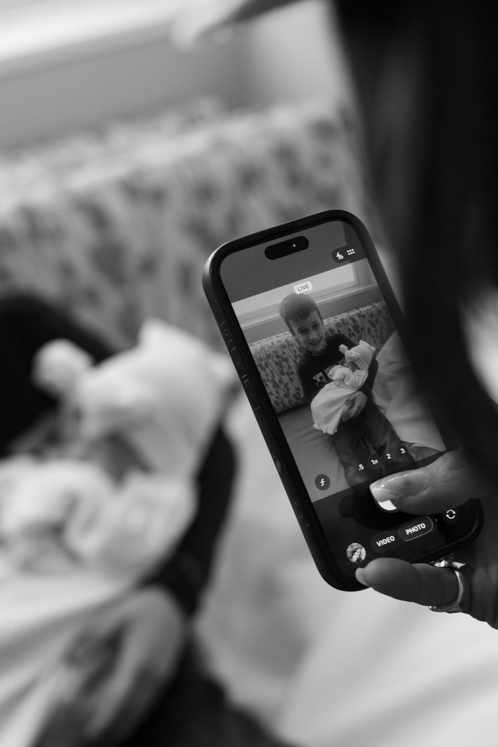 Black and white photo of a person holding a smartphone capturing a picture of a woman holding a newborn baby.