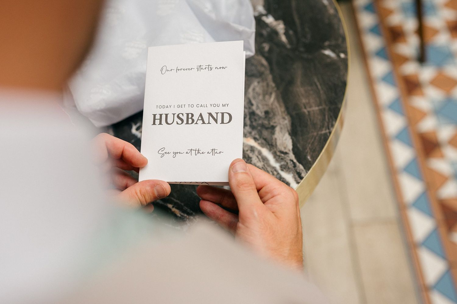 Person holding a wedding card addressed to husband with elegant typography at a marble table.