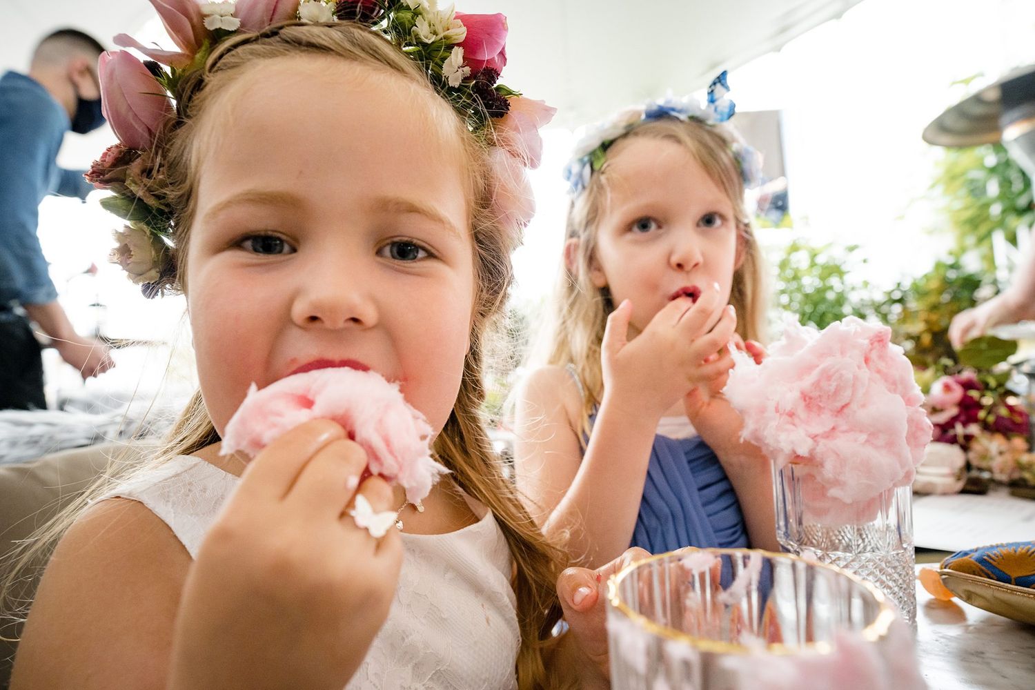Two young flower girls in floral crowns eating pink cotton candy at a wedding reception at Saraguay House