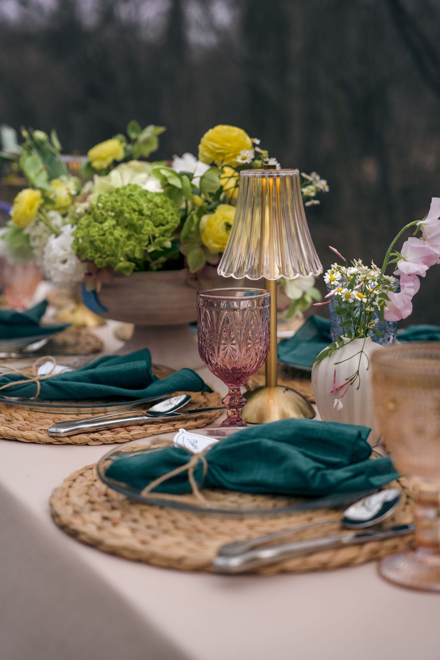 Elegant tablescape with teal napkins, woven placemats, floral centerpiece, and gold candlesticks on a neutral tablecloth.