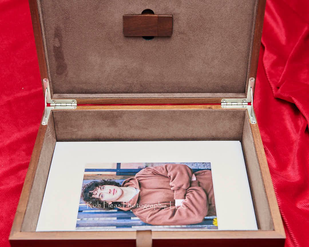 Premium walnut folio box with lid open, showing matching walnut memory card, fuzzy-lined interior, and sample mounted prints.