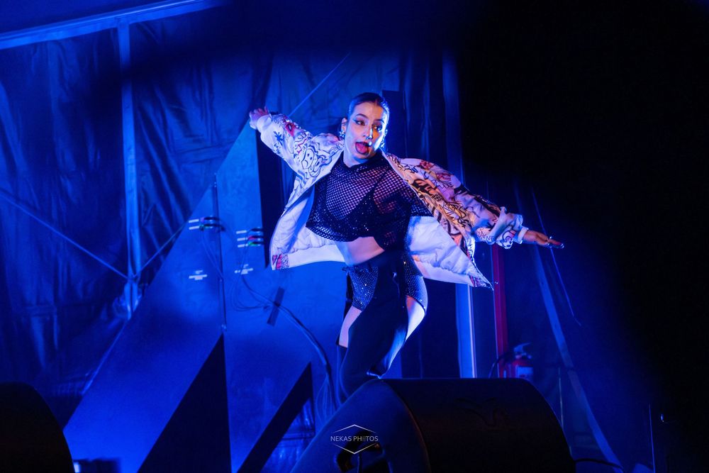 Performer in dramatic pose on stage under blue lighting wearing ornate costume.