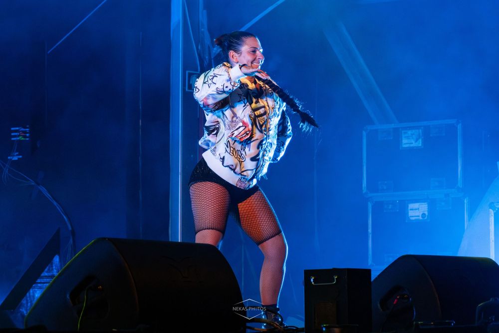 Female performer in colorful tiger jacket singing on stage under blue lights.