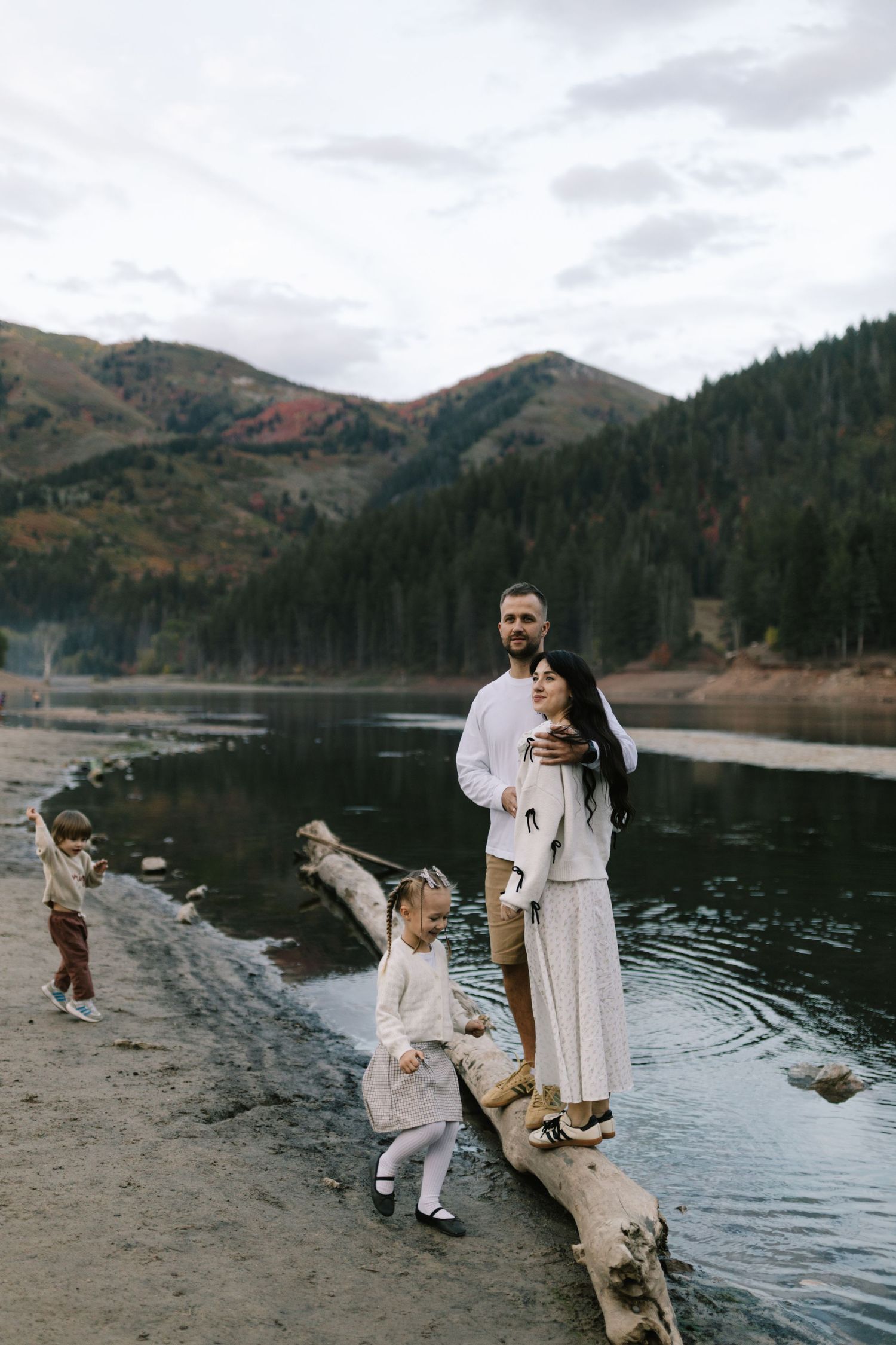 Family of four posing near a Tibble Fork reservoir Utah, mountain lake surrounded by autumn forest and rocky shoreline.