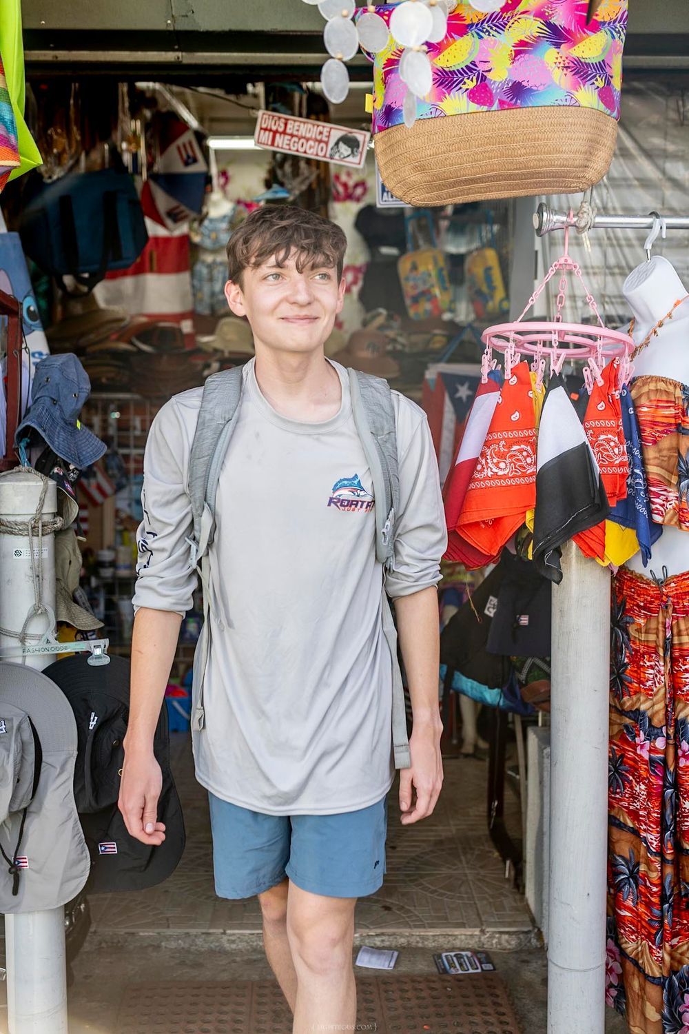 Young man with backpack smiling while standing in the entrance of a colorful souvenir shop.