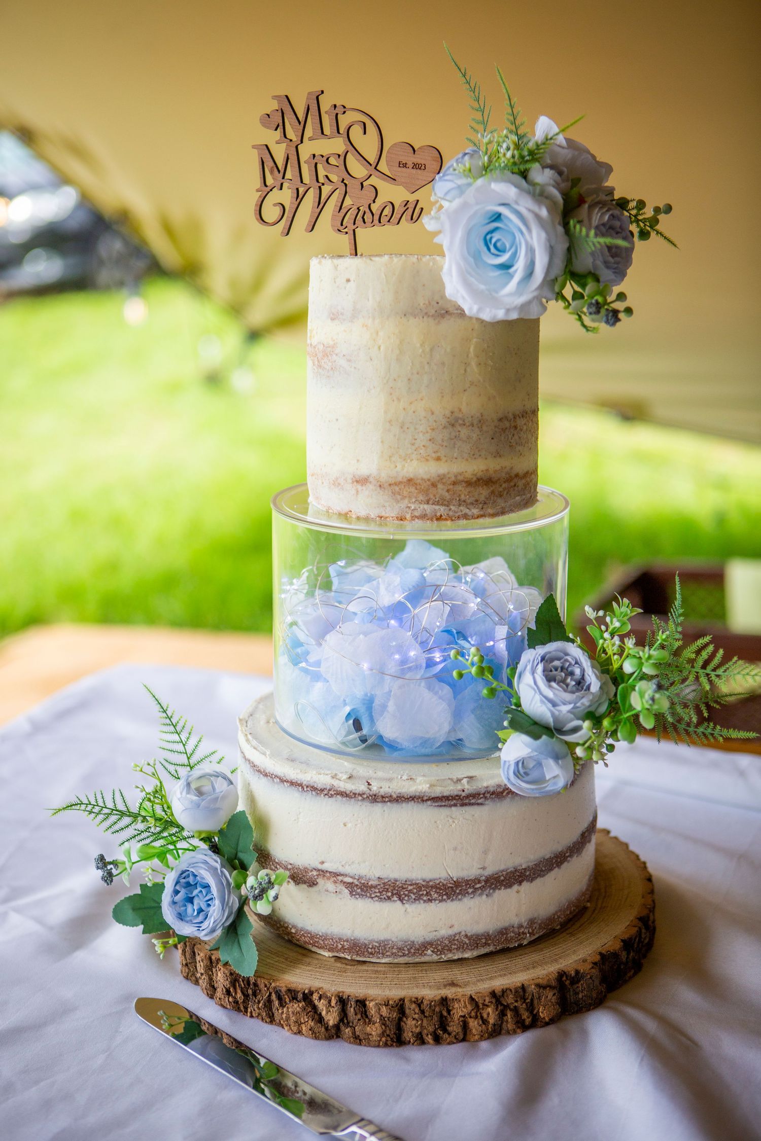 Elegant three-tier naked wedding cake with blue hydrangeas and Mr & Mrs Mason topper.