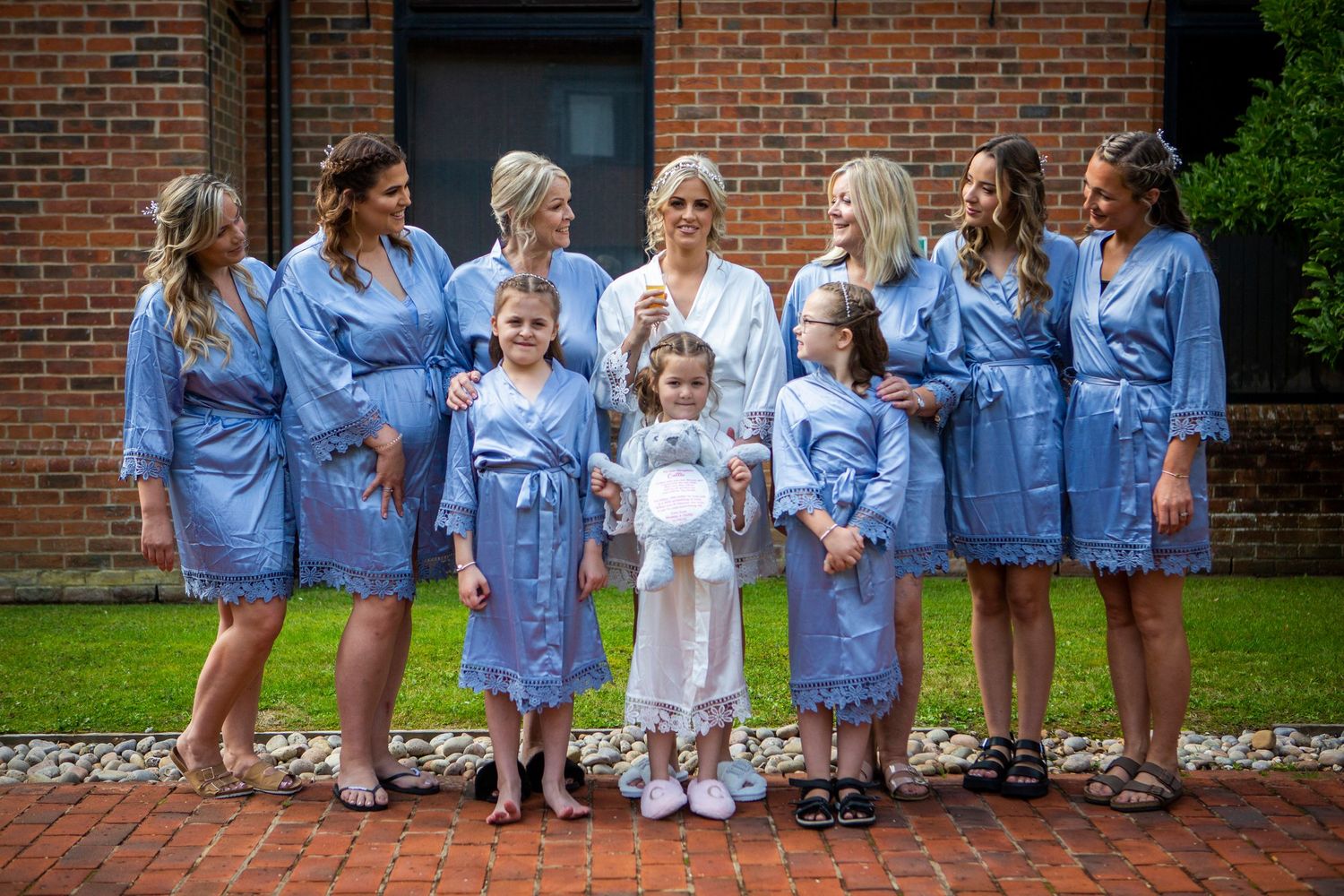 Bridal party in matching blue robes posing with flower girls outside brick building.