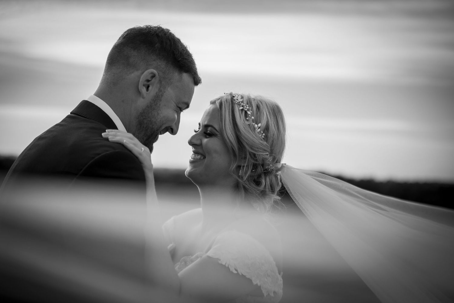 Romantic black and white portrait of bride and groom gazing at each other beneath a flowing veil.