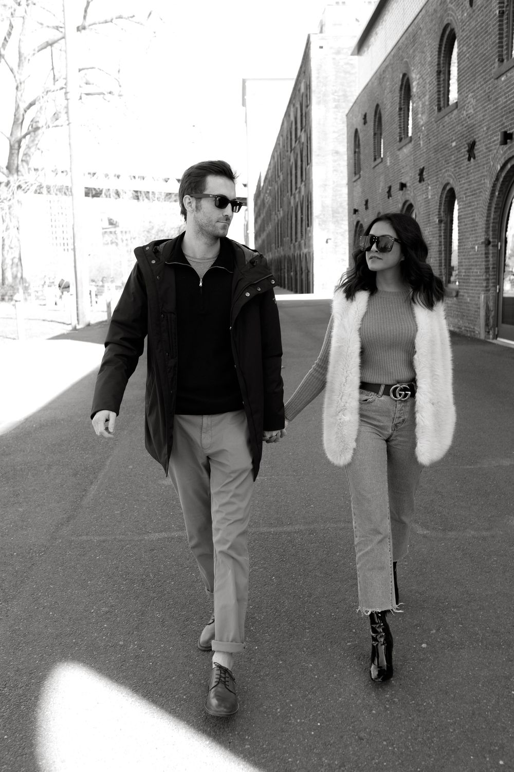 Couple holding hands walking in black and white photo near brick building.
