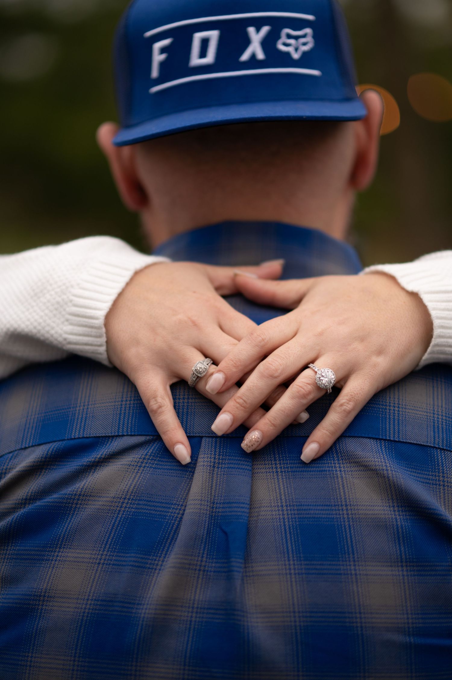 Close-up of couple embracing showing two diamond rings on womans hands on mans back.