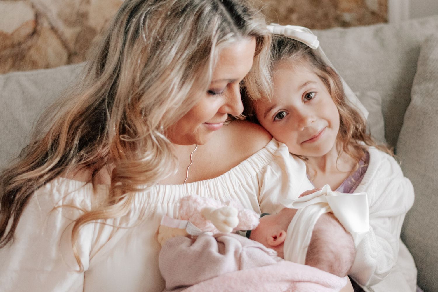 A mother holds a newborn baby while an older daughter in white dress smiles warmly during a family portrait session.
