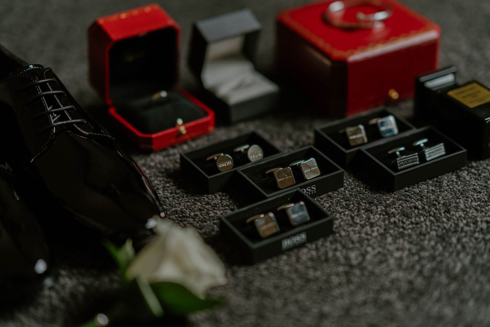 Wedding jewelry display featuring rings and cufflinks in red and black boxes arranged on a gray surface.