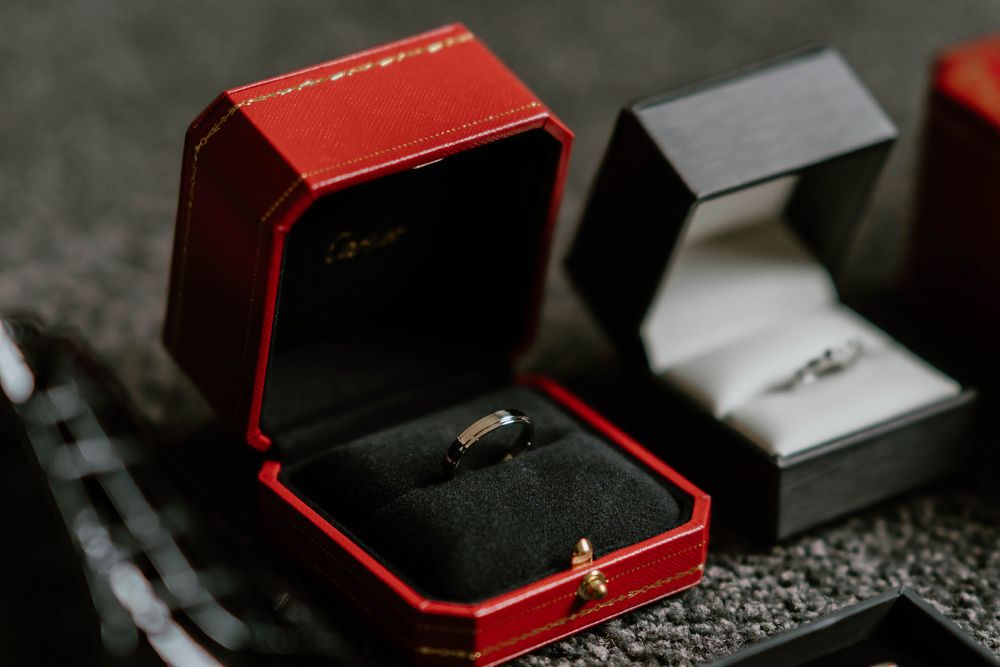 Two Cartier ring boxes displaying a gold wedding band and diamond engagement ring on a dark surface.