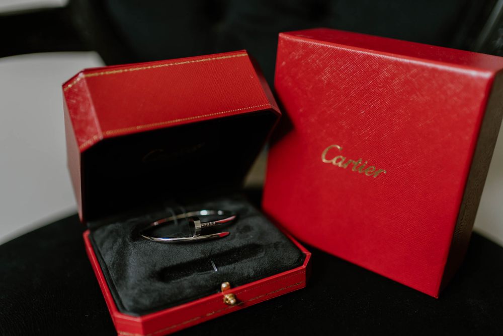 Cartier love bracelet in silver displayed in a red Cartier gift box with velvet interior on a dark surface.