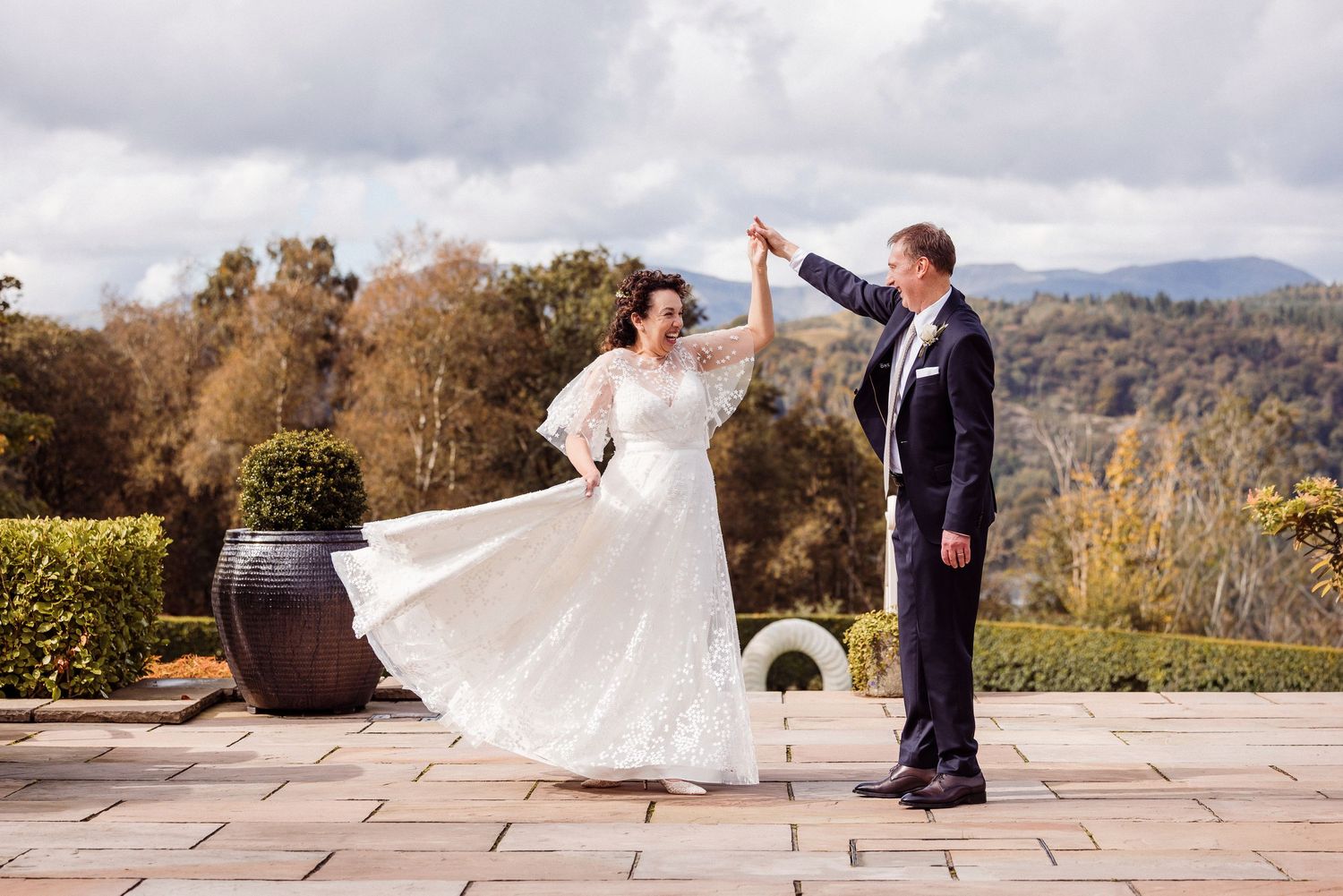 Bride and groom dancing outdoors on stone terrace with scenic mountain views on their wedding day.