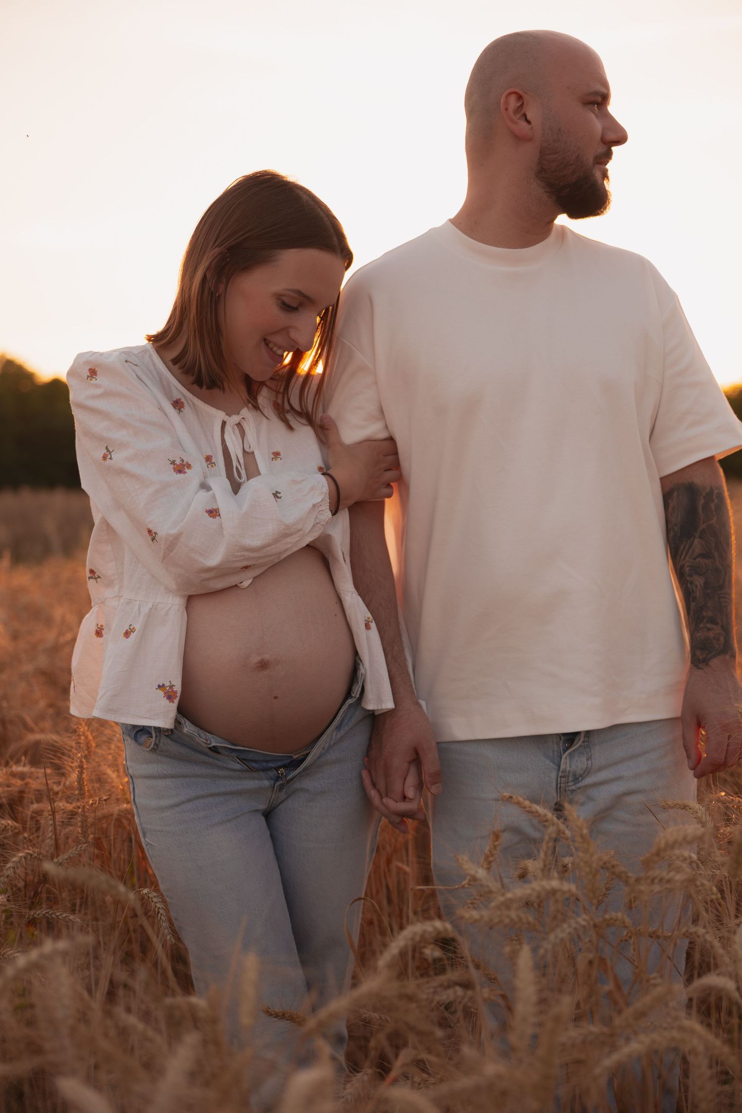 Portrait d'une femme enceinte debout dans un champ doré en Dordogne lors d'une séance photo grossesse lifestyle au coucher du soleil