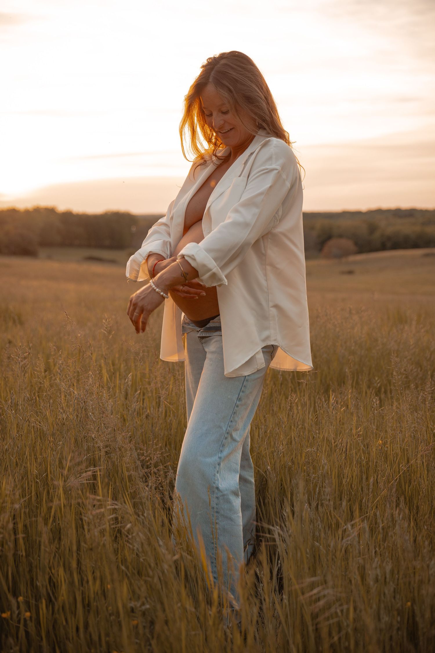 Portrait d'une femme enceinte debout dans un champ doré en Dordogne lors d'une séance photo grossesse lifestyle au coucher du soleil