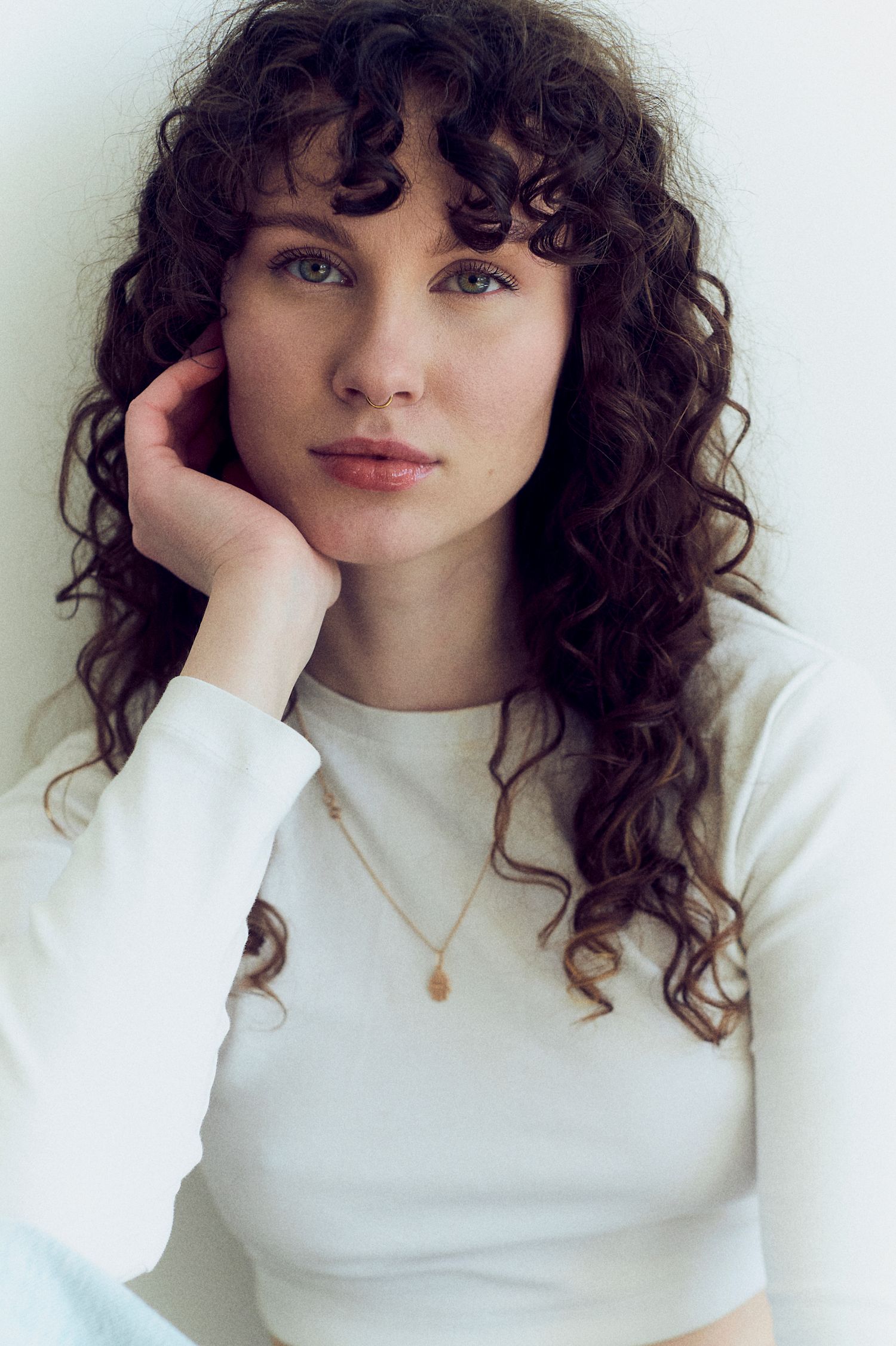 Black and white portrait of a young woman with curly hair, resting her chin on her hand while seated.