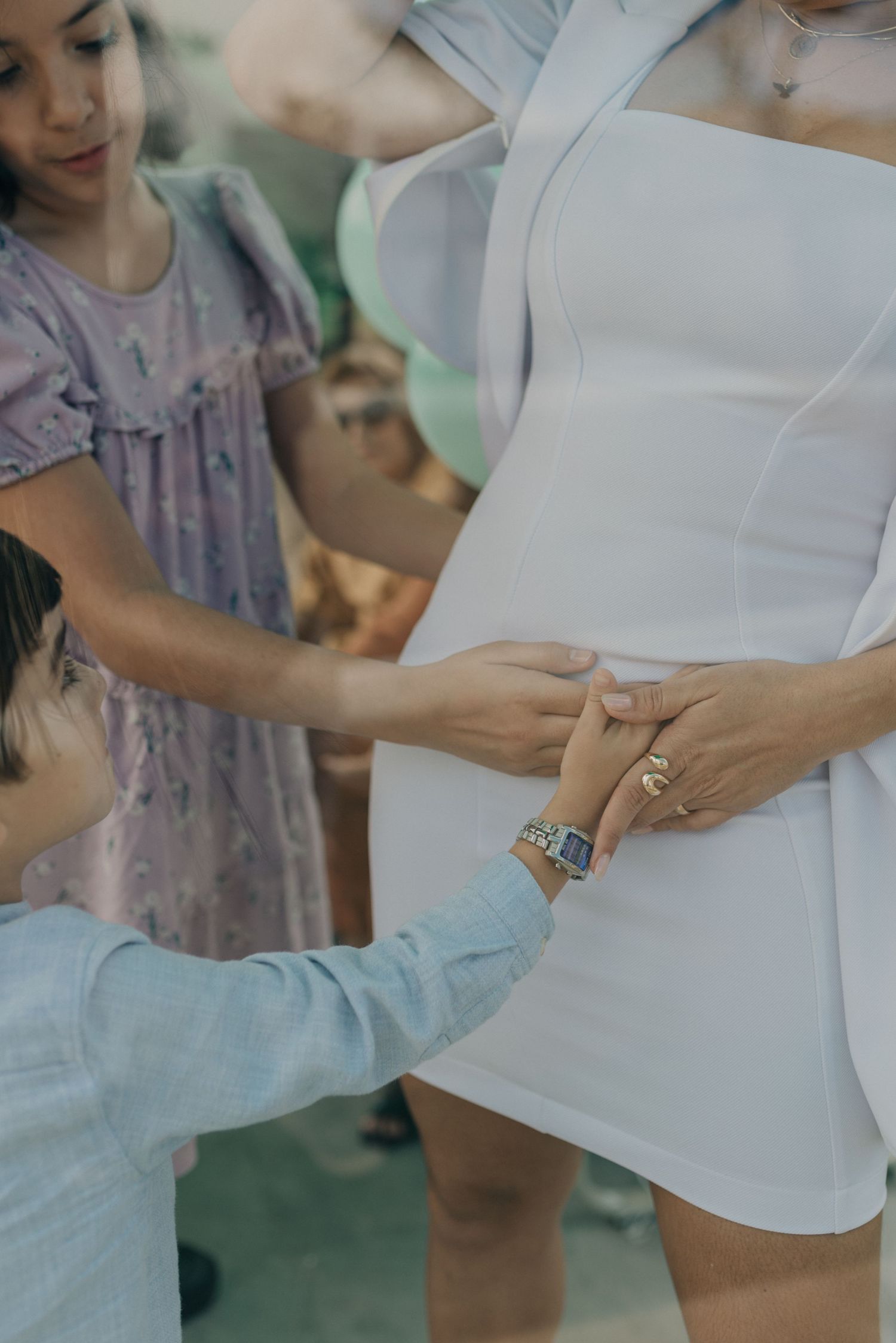 A touching moment at a baby gender reveal party as people gather around a pregnant belly in a white dress.
