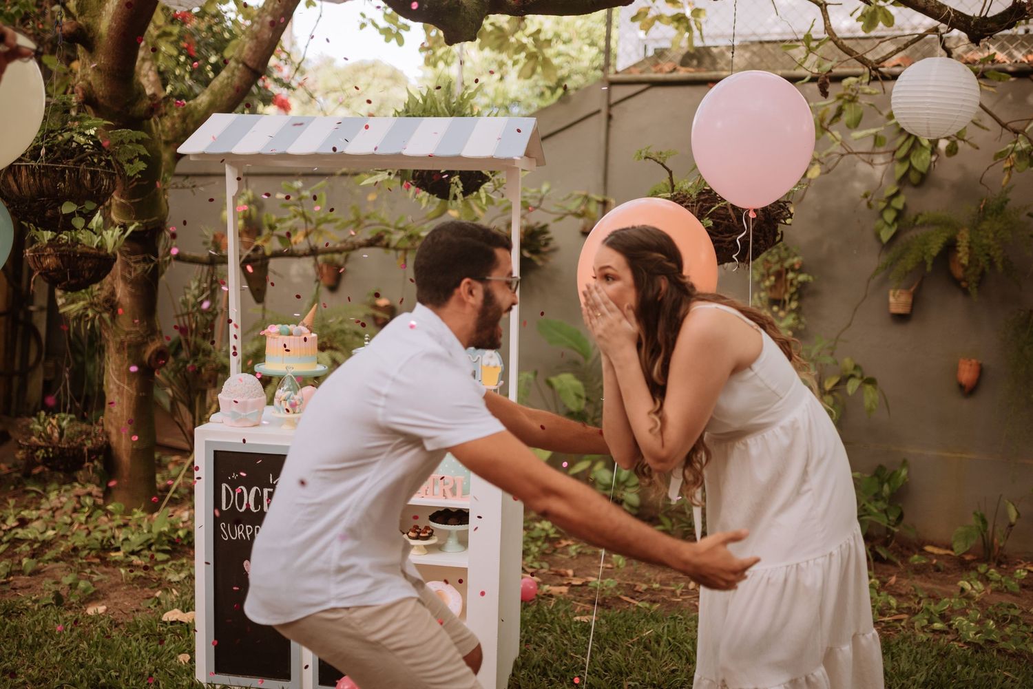 An emotional moment captured during a baby gender reveal celebration in a garden setting with balloons.