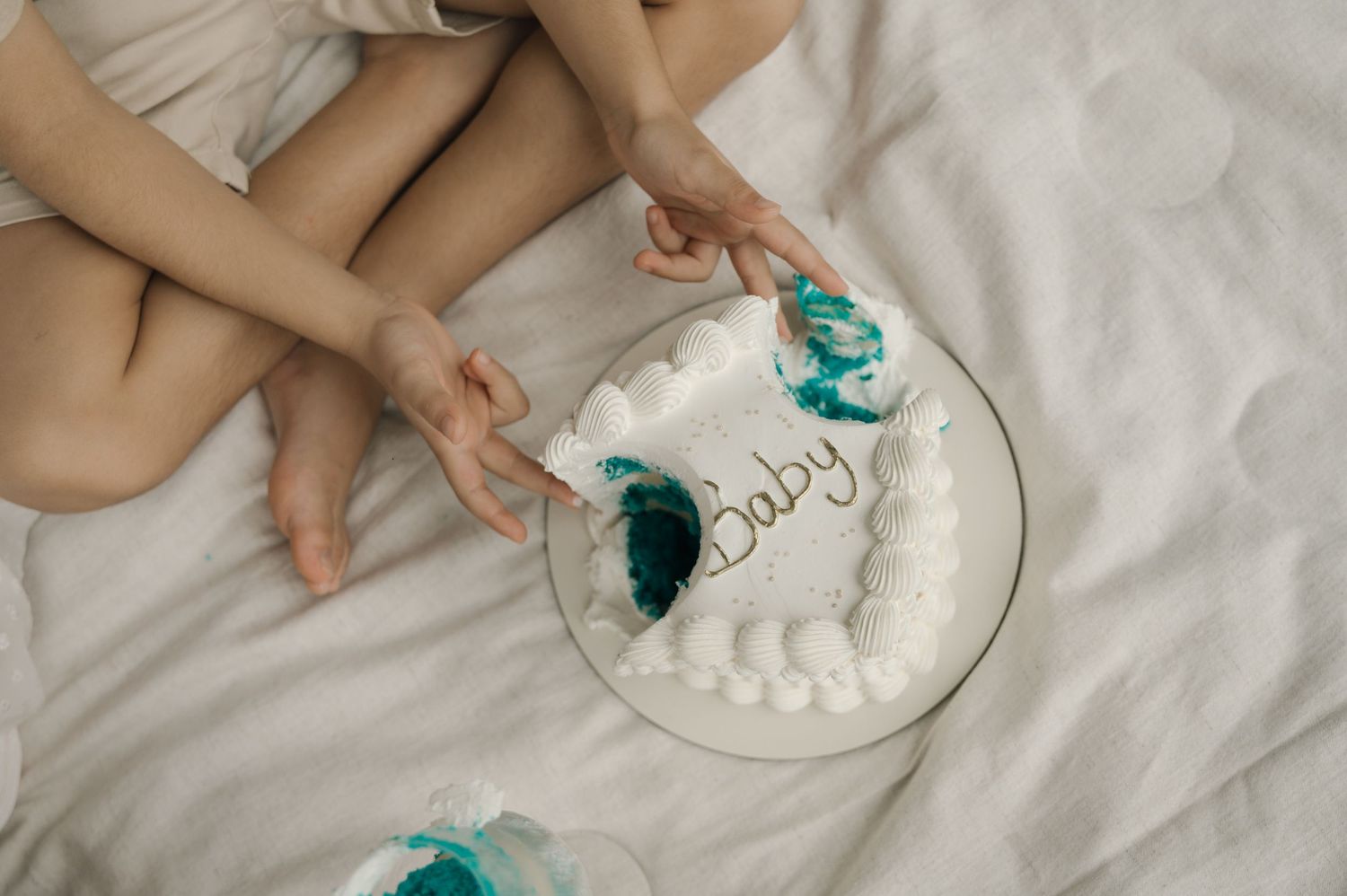 Overhead view of hands holding a white cake with Baby written on it on a white bed.