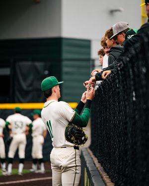 Baseball player in green uniform interacts with fans through the outfield fence during a game.