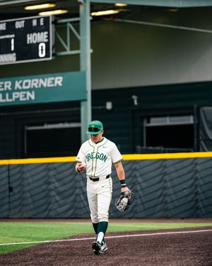 Oregon Ducks baseball player in white uniform walks on field at PK Park stadium during a game.