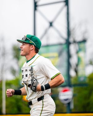 Baseball player in green and white uniform jogging on field wearing green cap and batting gloves.