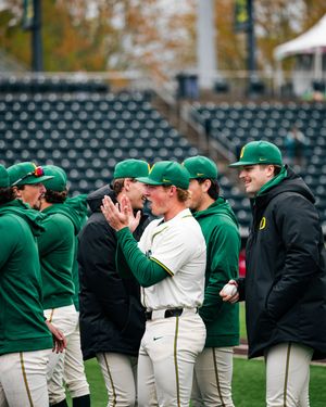 Oregon Ducks baseball players in green uniforms laugh and chat on the field during a pre-game gathering.