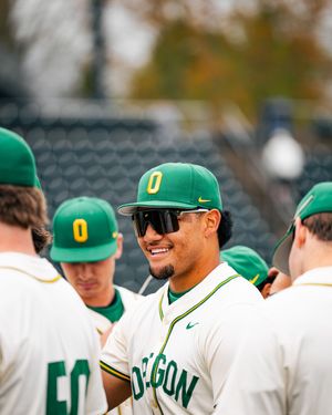 Oregon Ducks baseball players in green and white uniforms huddle together smiling on the field during a game day.