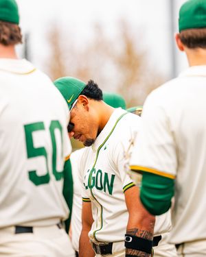 Oregon Ducks baseball players in white and green uniforms huddle together on the field during a game.
