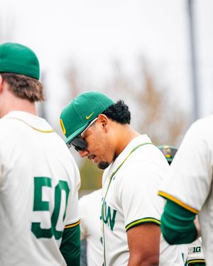 Oregon Ducks baseball players in green and white uniforms huddle together during a game.