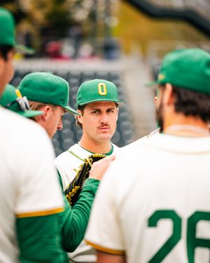 Oregon Ducks baseball players huddle in green and white uniforms during a game discussion on the field.