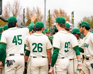 Oregon Ducks baseball players in white uniforms with green trim celebrate together after game.