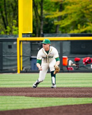 Oregon Ducks baseball player in green and yellow uniform fielding position on the infield dirt during a college game.