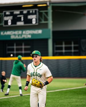 Oregon Ducks baseball player in green uniform and sunglasses stands on field during warm-ups at Karcher Korner Bullpen.