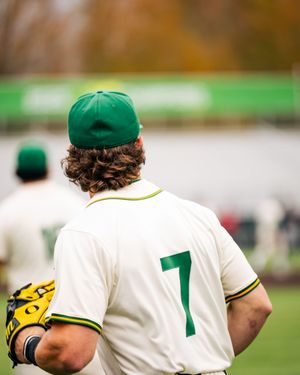 Baseball player wearing number 7 green and white uniform with green cap holding glove on autumn day.