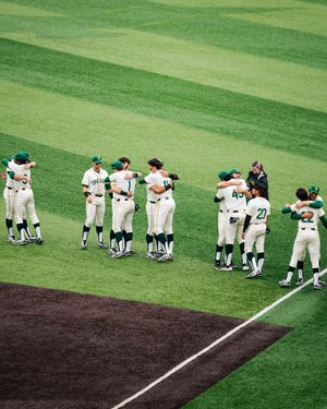 Baseball team in white and green uniforms hugging each other on a green field after a game.