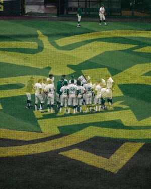 Oregon Ducks baseball team huddles together on the field during a game at a stadium with green turf.