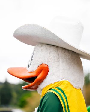 University of Oregon Duck mascot in green and yellow uniform wearing a white cowboy hat outdoors.