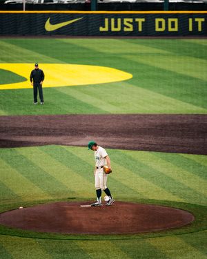 Oregon Ducks baseball pitcher stands on the mound at PK Park with Nike Just Do It sign in background.