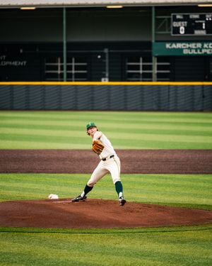 Baseball pitcher in white and green uniform winds up to deliver a pitch on the mound.