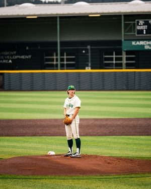 A baseball pitcher stands on the mound in a green and white uniform, holding his glove at a professional stadium.