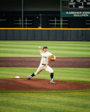 College baseball pitcher in Oregon green uniform releases a pitch during a home game.