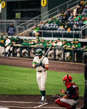 Oregon Ducks baseball batter stands ready at home plate while a catcher crouches behind during a college game.