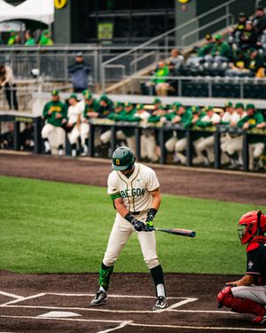 Oregon Ducks baseball player in green helmet and uniform stands at bat during a college baseball game.