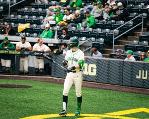 Oregon Ducks baseball player in green uniform stands at bat during a college game at a packed stadium.